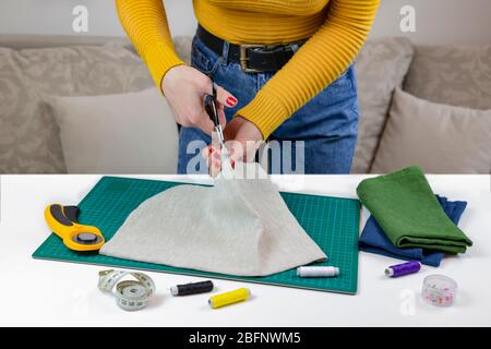 woman in a yellow cuts the fabric. there are quilting tools on the table. patchwork knife, scissors, lined cutting mat, self-locking, thread, centimet Stock Photo