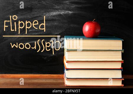 Flipped classroom concept. Books and apple on blackboard background Stock Photo