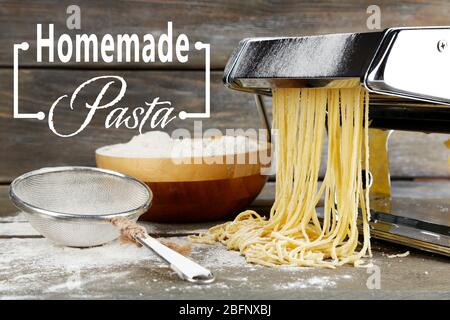 Raw homemade pasta, sieve and machine on wooden background Stock Photo