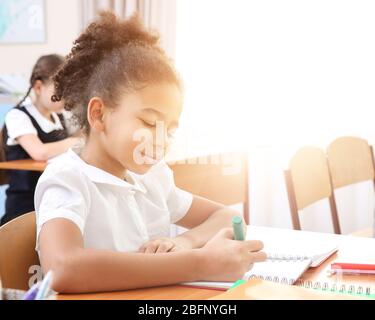 Little African-American girl doing homework at table in classroom Stock Photo