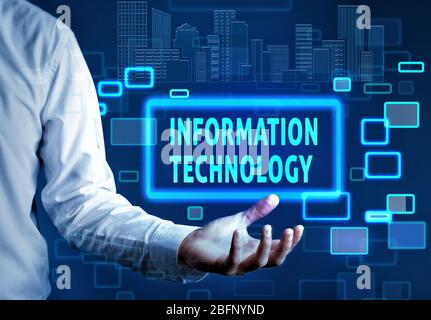 Businessman holding virtual icon with text INFORMATION TECHNOLOGY against dark background Stock Photo
