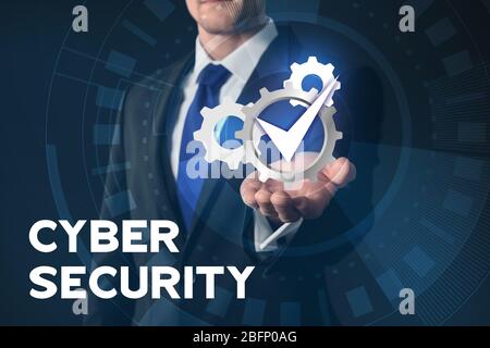Businessman holding virtual gears and check mark against dark background. Concept of cyber security and attack Stock Photo