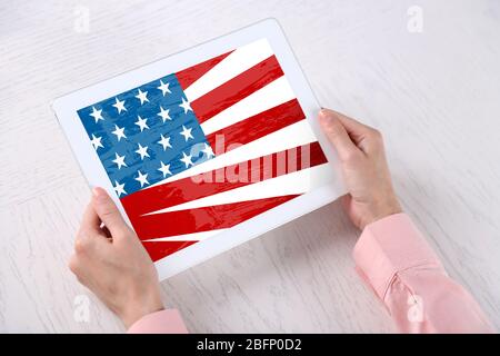 Young woman holding tablet with American flag on screen over table Stock Photo