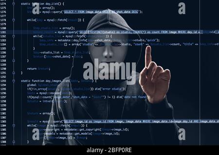 Hacker in mask working with virtual screen against dark background. Concept of cyber security and attack Stock Photo