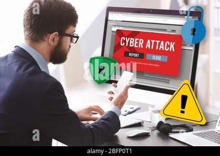 Man with smartphone and computer at table. Notification about threat of cyber attack on screens Stock Photo