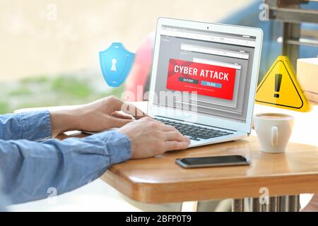 Man with laptop and notification about threat of cyber attack on screen at table Stock Photo