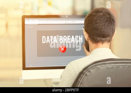 Man with computer and notification about threat of cyber attack on screen at table Stock Photo