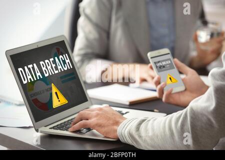Man with smartphone and computer at table. Notification about threat of cyber attack on screens Stock Photo