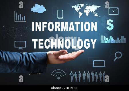 Businessman holding virtual text INFORMATION TECHNOLOGY against dark background Stock Photo