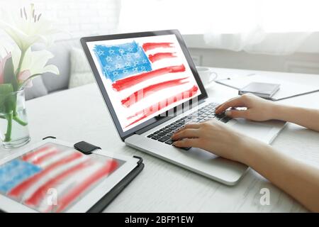 Young woman using laptop with American flag on screen at table Stock Photo