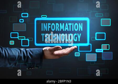 Businessman holding virtual icon with text INFORMATION TECHNOLOGY against dark background Stock Photo