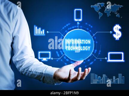 Businessman holding virtual icons and text INFORMATION TECHNOLOGY against dark background Stock Photo