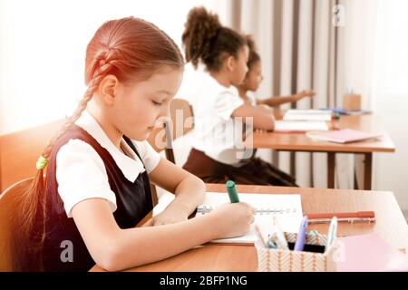 Little girl doing homework at table in classroom Stock Photo
