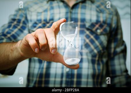 Young man holding hourglass in hand on grey background Stock Photo