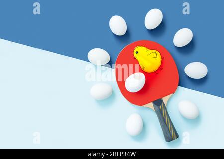 It could have been a chicken. A red table tennis racket is lying on blue table. There are identical eggs around racket.  Stock Photo