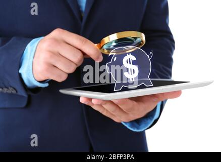 Businessman holding magnifying glass and digital tablet with virtual piggy bank Stock Photo