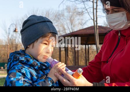 A small boy with illness bronchial asthma getting treatment with aerosol inhaler from his mama outdoors Stock Photo