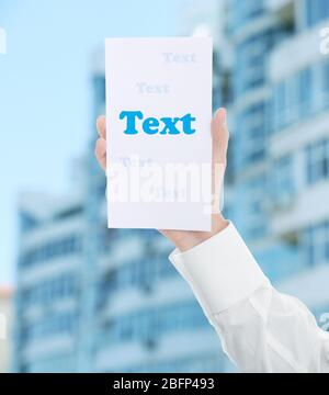 Male hand with white paper on multi-storey building blurred background Stock Photo
