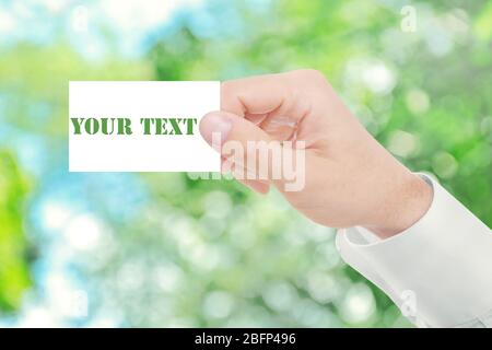 Male hand with white blank card on abstract nature blurred background Stock Photo