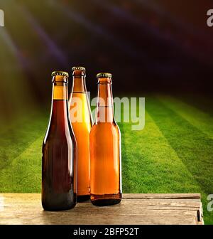 Beer bottles on wooden table against football field stadium background Stock Photo