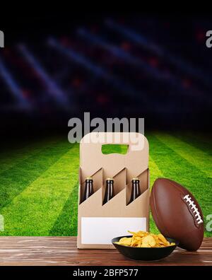 Six pack of beer, ball and snack on football field with spotlights Stock Photo