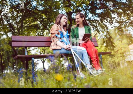 Two friends in a park, one with a broken feet and crutches Stock Photo