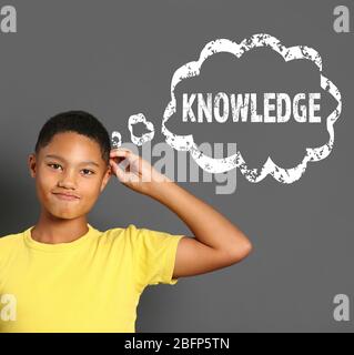 Cute afro american teenager with thought bubble and text knowledge on gray background. School concept. Stock Photo