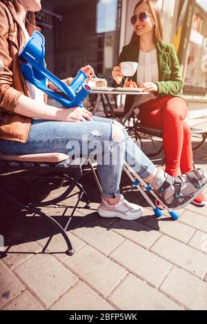 Two women, one with a broken leg and crutches, in a cafe Stock Photo