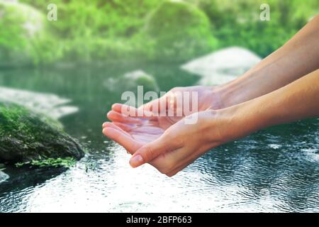 Clear natural water in woman hands on beautiful landscape background. Stock Photo