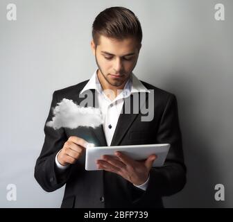 Businessman using tablet on gray background. Cloud computing and information storage concept. Stock Photo