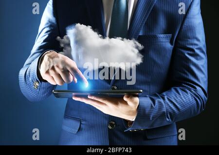 Businessman using tablet on blue background. Cloud computing and information storage concept. Stock Photo