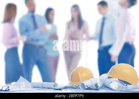 Helmets with blueprints on table and engineers on background Stock Photo