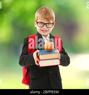 Little boy with backpack holding books and apple on blurred green background. School concept. Stock Photo