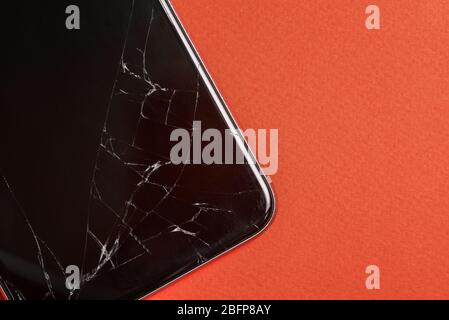 Broken glass of the phone screen. Black mobile phone with a broken screen. Smartphone on a red background close-up. Top view, flat lay Stock Photo