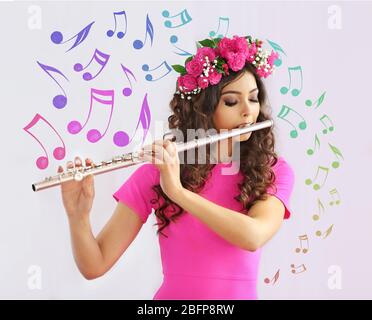 Beautiful young woman with flute. Musical notes design on light background. Stock Photo