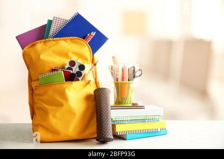 Yellow backpack with school supplies on wooden table against blurred background. School concept. Stock Photo