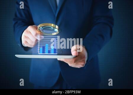 Businessman holding magnifying glass and tablet. Digital diagram on screen. Technology concept. Stock Photo