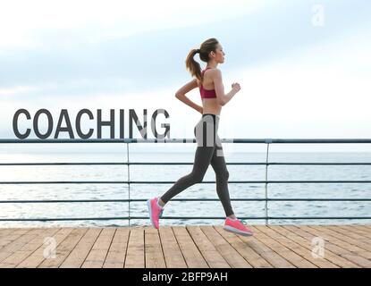 Word COACHING on background. Business trainer concept. Young woman running on pier Stock Photo