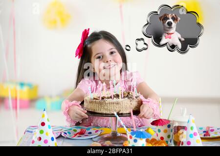 Happy little girl with tasty cake at birthday party dreaming about the dog Stock Photo