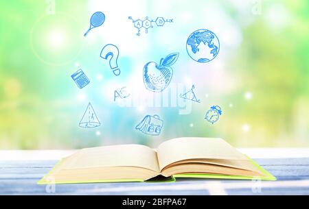 Book on wooden table. Icons on blurred green background. Knowledge concept. Stock Photo