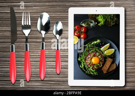 Table appointments and tablet. Photo of food on tablet screen. Stock Photo