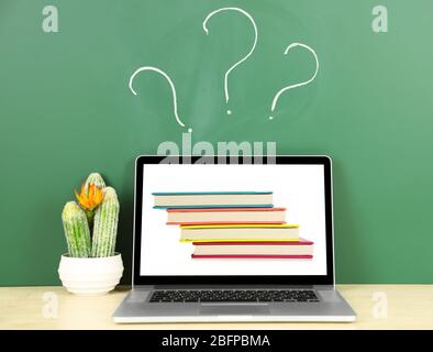 Laptop with stack of notebooks wallpaper on screen against chalkboard. Question mark on background. School teacher concept. Stock Photo