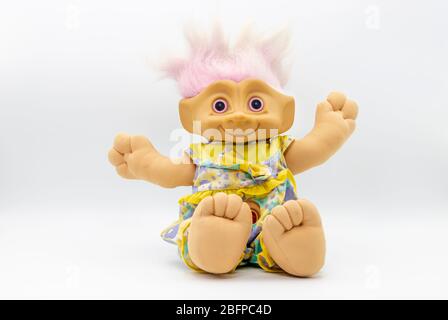 Vintage child's cuddly toy: a smiling plastic troll with pink eyes and purple hair, outstretched arms in a sitting position against a white background Stock Photo