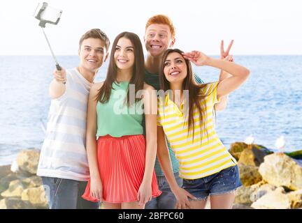 Group of young people taking selfie on blurred ocean background. Stock Photo