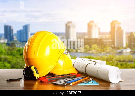 Construction blueprints with tools and helmets on cityscape background Stock Photo