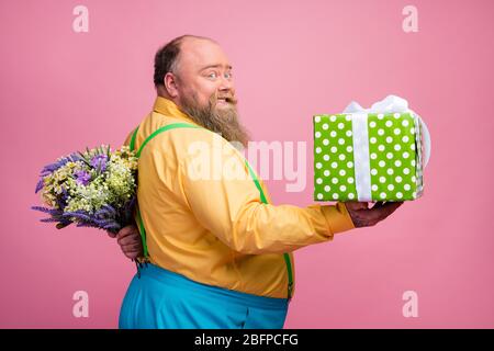 Profile side view portrait of his he nice romantic careful funky glad bearded guy giving you giftbox hiding flowers behind back congratulating Stock Photo