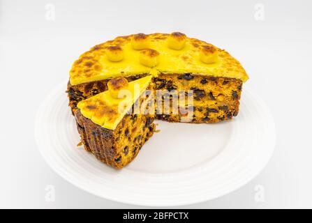 Traditional home baked simnel cake with a cut slice on a white plate for Easter - fruit cake topped with toasted yellow marzipan topping and balls Stock Photo