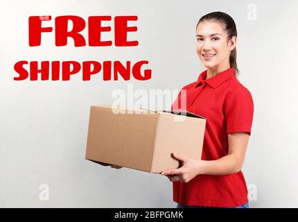 Delivery concept. Young woman holding parcel and text FREE SHIPPING on gray background Stock Photo