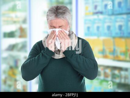 Allergies or cold concept. Senior man blowing nose on tissue at pharmacy Stock Photo