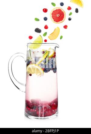 Falling fruit slices and berries into glass jug with lemonade on white background. Recipe for summer drink Stock Photo